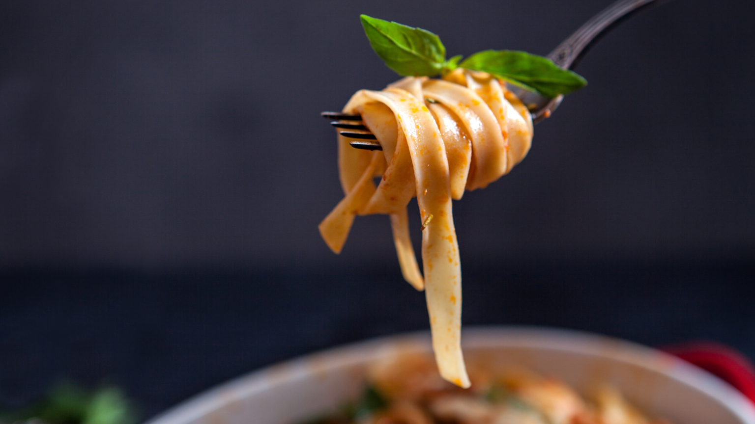 Una forchetta con tagliatelle arrotolare e del basilico sopra