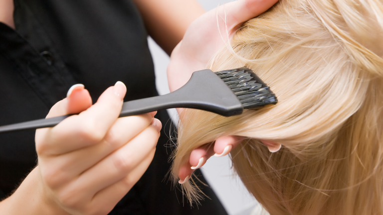 Il dettaglio di una ciocca di capelli bionda e un pennello per la tinta