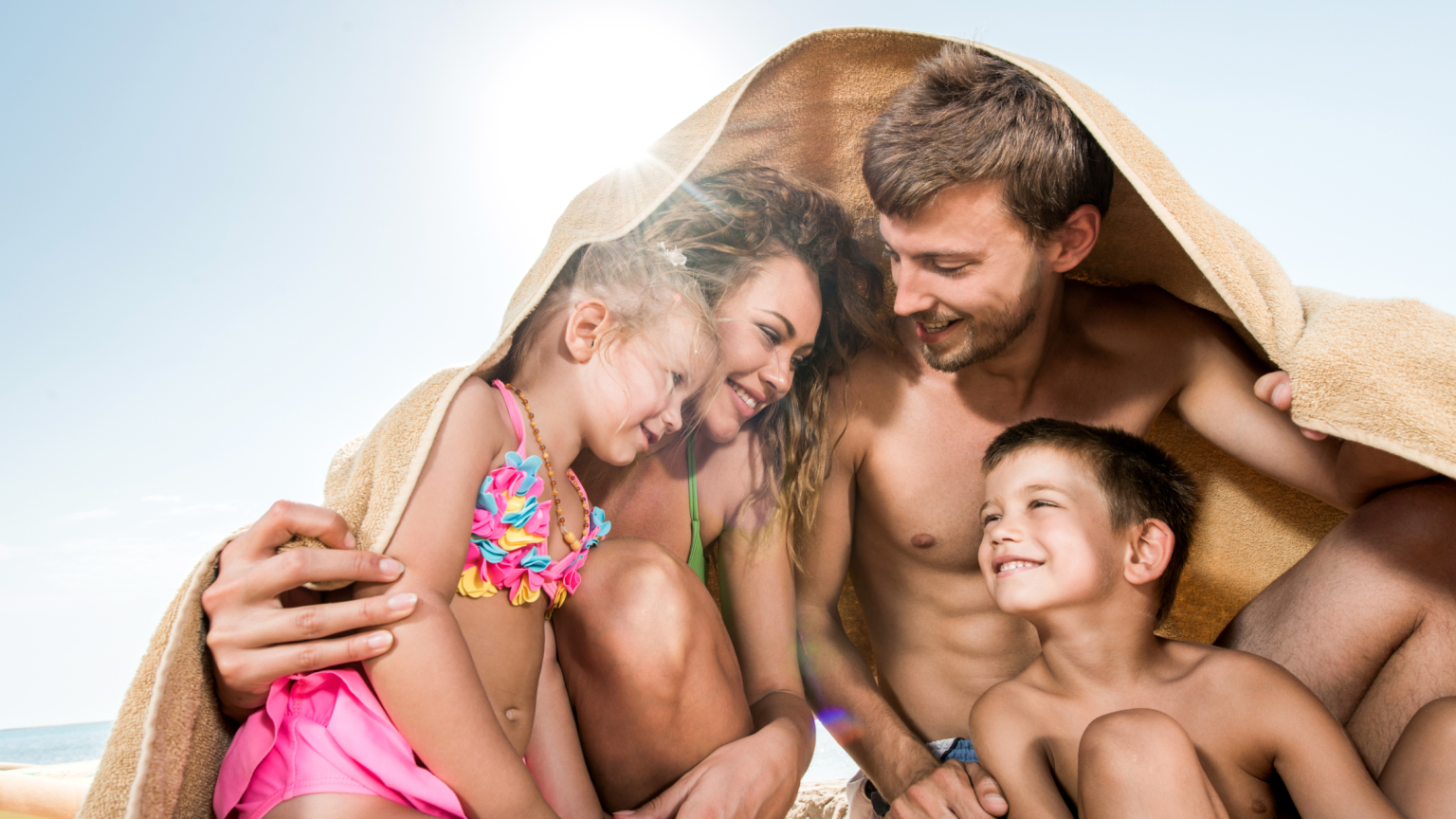 Papà mamma e due figli in spiaggia sotto un telo mare che sorridono