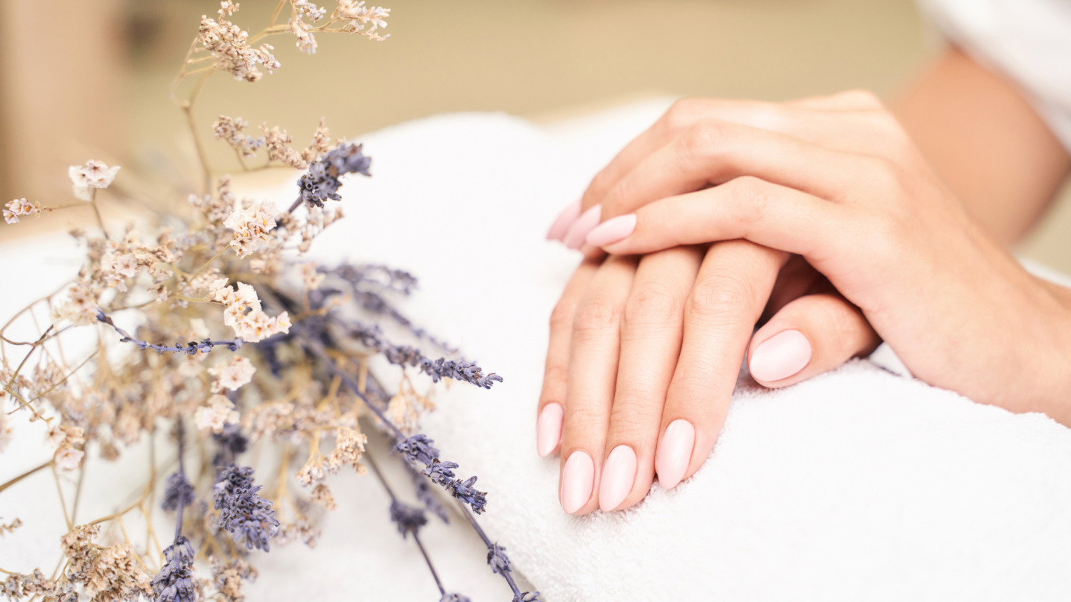 Delle mani con smalto semipermanente e dei fiori secchi come scenografia
