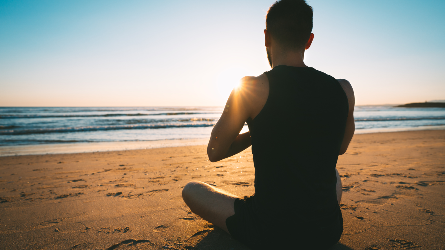 Un ragazzo che fa meditazione sulla spiaggia all'alba