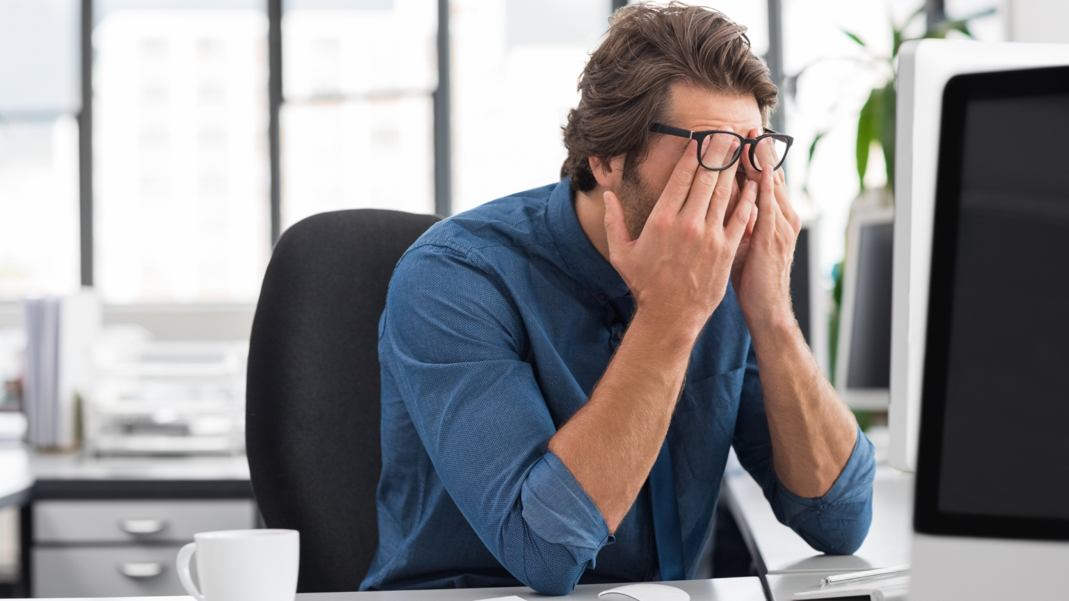 Un ragazzo in ufficio con le mani sul volto
